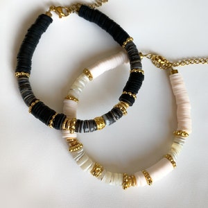 May include: Two bracelets with gold accents. One bracelet is black and white, the other is white and pink.