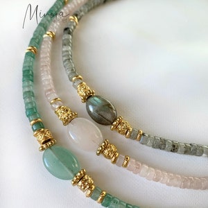 May include: A layered necklace with green, grey, and pink beads. The necklace features gold accents and three larger stones: a green stone, a pink stone, and a grey stone.