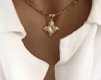 May include: A gold necklace with a delicate chain and a small, ornate cross pendant. The necklace is made of tiny brown beads and is worn by a person with a white shirt.