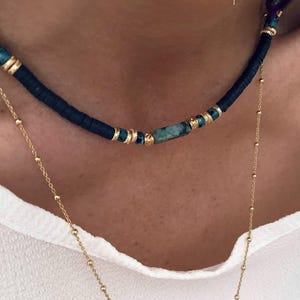 以下が含まれることがあります： 黒とターコイズのビーズネックレスで、ゴールドのアクセントが施されています。ネックレスの中央には長方形のターコイズストーンが飾られています。