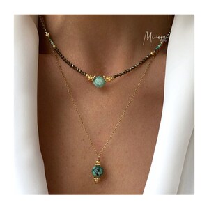 May include: Two gold necklaces with turquoise beads. The top necklace is a choker with small brown beads and a larger turquoise bead. The bottom necklace has a larger turquoise bead pendant.