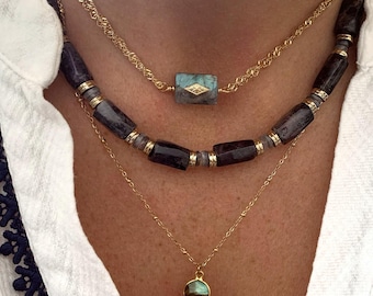 May include: Layered gold chain necklaces with a turquoise gemstone pendant and a black and grey beaded necklace with a green gemstone pendant.