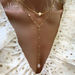 May include: A gold chain necklace with two pearls and a delicate design. The necklace is layered with a shorter chain with a pearl in the centre.