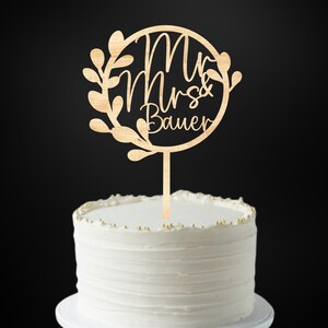 Op de afbeelding: Houten taarttopper met een cirkel en bladeren, met de tekst "Mr & Mrs Bauer".