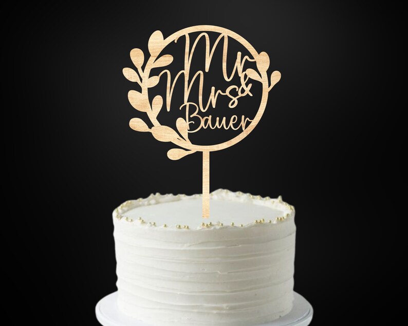 Op de afbeelding: Houten taarttopper met een cirkel en bladeren, met de tekst "Mr & Mrs Bauer".