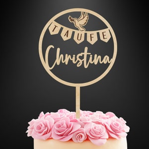 K&ouml;nnte beinhalten: Ein runder Tortenstecker aus Holz mit einer lasergeschnittenen Taube, die einen Olivenzweig h&auml;lt, &uuml;ber einem Banner mit dem Text TAUFE und dem Namen Christina in Schreibschrift, befestigt an einem Stab in einer Torte mit rosa Rosen.