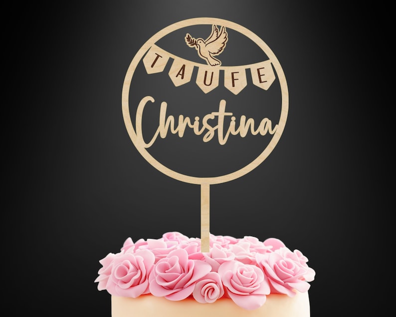 K&ouml;nnte beinhalten: Ein runder Tortenstecker aus Holz mit einer lasergeschnittenen Taube, die einen Olivenzweig h&auml;lt, &uuml;ber einem Banner mit dem Text TAUFE und dem Namen Christina in Schreibschrift, befestigt an einem Stab in einer Torte mit rosa Rosen.