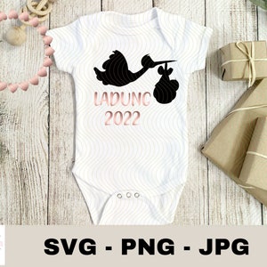 May include: White baby onesie with a black stork silhouette carrying a baby bundle. The text "LADUNG 2022" is printed in pink on the onesie.
