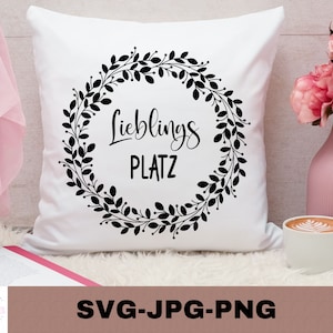 May include: White pillow with a black wreath design and the text "Lieblings Platz" in a cursive font.