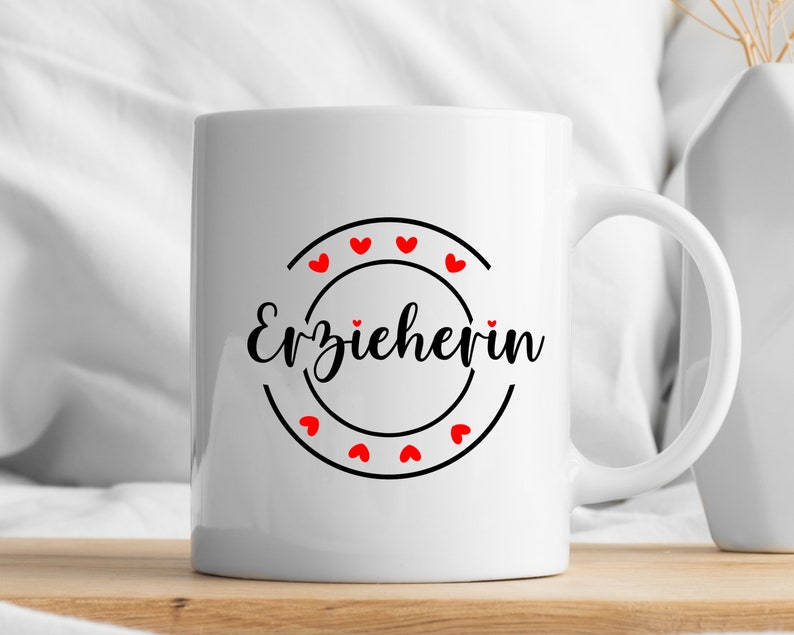 May include: White ceramic mug with a black circle and the text "Erzieherin" in black script. The circle is decorated with red hearts.