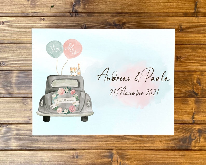May include: A watercolor print featuring a gray vintage car decorated with a floral wreath and a Just Married banner. Above the car are two balloons labeled Mr and Mrs, two champagne flutes, and a bottle. Text reads Andreas & Paula 21. November 2021.
