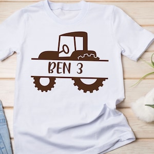 May include: White t-shirt with a brown tractor design and the name "BEN 3" printed on a banner.