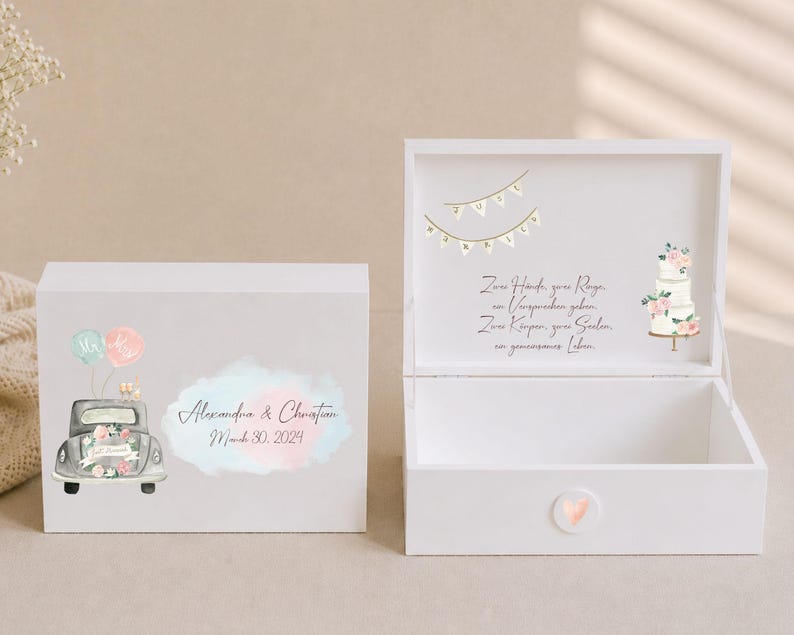 May include: A white wooden keepsake box featuring a watercolor illustration of a vintage car with balloons, the names Alexandra & Christian, and the date March 30, 2024. The open lid displays a wedding cake, bunting, and German text.