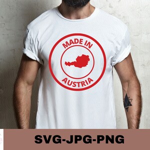 Op de afbeelding: Wit T-shirt met een rode cirkelvormige afbeelding met de tekst "Made in Austria" en een omtrek van Oostenrijk in rood.