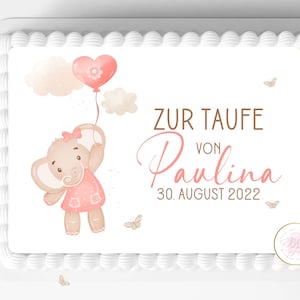 May include: A white cake with a pink elephant holding a pink heart balloon. The cake is decorated with a brown text that says "Zur Taufe von Paulina 30. August 2022".