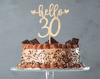 Może przedstawiać: Ciasto czekoladowe z czekoladowymi posypkami i drewnianym topperem na tort z napisem "hello 30".
