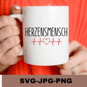 May include: White ceramic mug with a black and red design. The mug says "HERZENSMENSCH" with a red heart and a heartbeat line.
