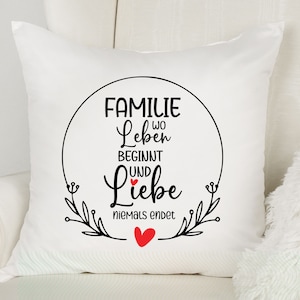 May include: White throw pillow with black text that reads "Familie wo Leben beginnt und Liebe niemals endet" with a small red heart in the middle of the text. The text is inside a circle with a floral design.