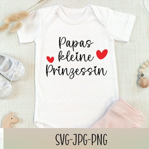 Pode incluir: Macacão branco para bebé com texto preto que diz "Papas kleine Prinzessin" com dois corações vermelhos.