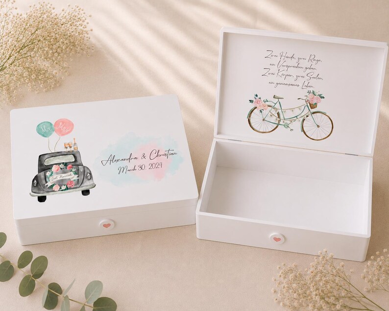 May include: Two white wooden keepsake boxes with hinged lids. The closed box features a watercolor illustration of a car with balloons and the text Alexandra & Christian March 30, 2024. The open box shows a bicycle illustration and German text.