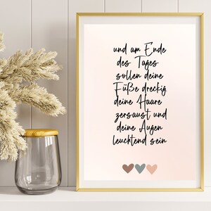 May include: A framed print with a pink background and white text that reads "und am Ende des Tages sollen deine F&uuml;&szlig;e dreckig deine Haare zersaust und deine Augen leuchtend sein". Three small hearts are at the bottom of the print, one brown, one gray, and one pink.