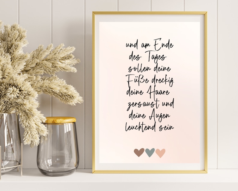 May include: A framed print with a pink background and white text that reads "und am Ende des Tages sollen deine F&uuml;&szlig;e dreckig deine Haare zersaust und deine Augen leuchtend sein". Three small hearts are at the bottom of the print, one brown, one gray, and one pink.