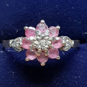 May include: A silver ring featuring a pink flower-shaped centre made of small pink stones surrounded by smaller white stones.