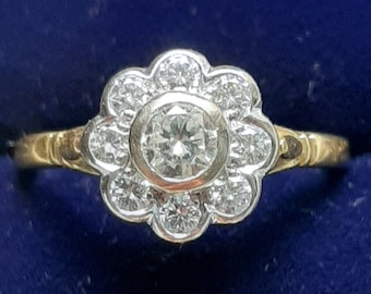 May include: A gold ring with a flower-shaped setting of diamonds. The center stone is a large round diamond.