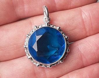 Peut inclure: Un pendentif en argent avec une grande pierre précieuse bleue facetée sertie dans une bélière en argent. Le pendentif a un bord décoratif perlé.