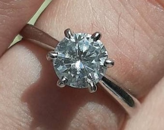May include: A silver ring with a large, round, clear diamond set in a six-prong setting.