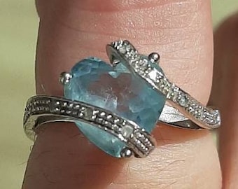 May include: A silver ring with a large blue heart-shaped gemstone surrounded by smaller clear gemstones.