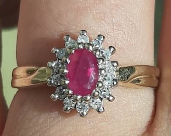 Pode incluir: Um anel de ouro com uma grande rubi ovalada cercada por diamantes menores.