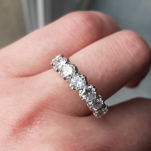 May include: A silver band with a row of round, clear gemstones set in a prong setting.