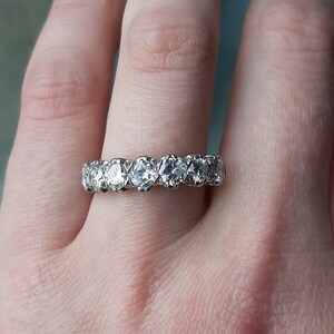 May include: A silver band ring with a row of round, clear gemstones.