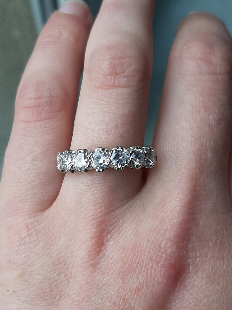 May include: A silver band ring with a row of round, clear gemstones.