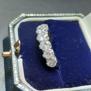 May include: A silver band ring with a row of five round, clear diamonds set in a prong setting.