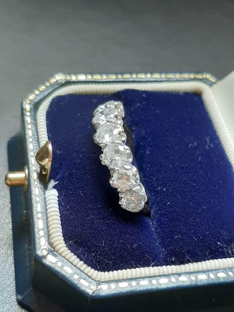 May include: A silver band ring with a row of five round, clear diamonds set in a prong setting.