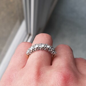 May include: A silver band ring with a row of round, clear diamonds set in a pave setting.