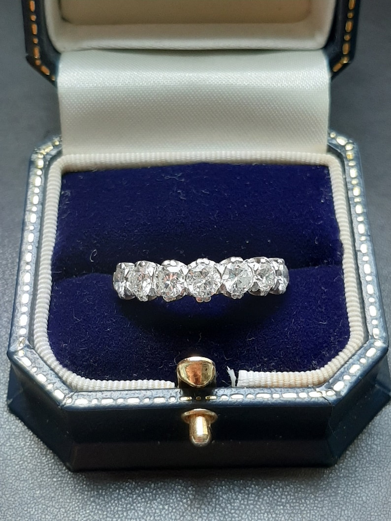 May include: A silver ring with a row of round, clear diamonds set in a band. The ring is in a blue velvet ring box.