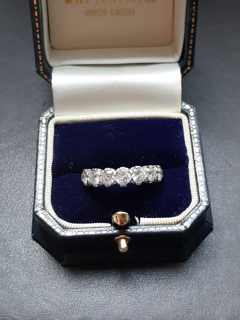 May include: A diamond eternity band ring in a blue velvet ring box. The ring is set with round brilliant diamonds.