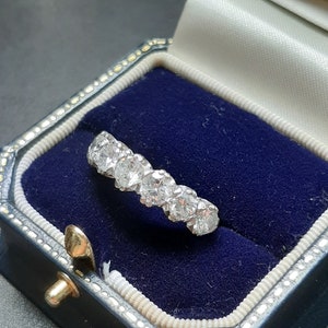 May include: A silver ring with a row of round, clear diamonds set in a band. The ring is in a blue velvet ring box.