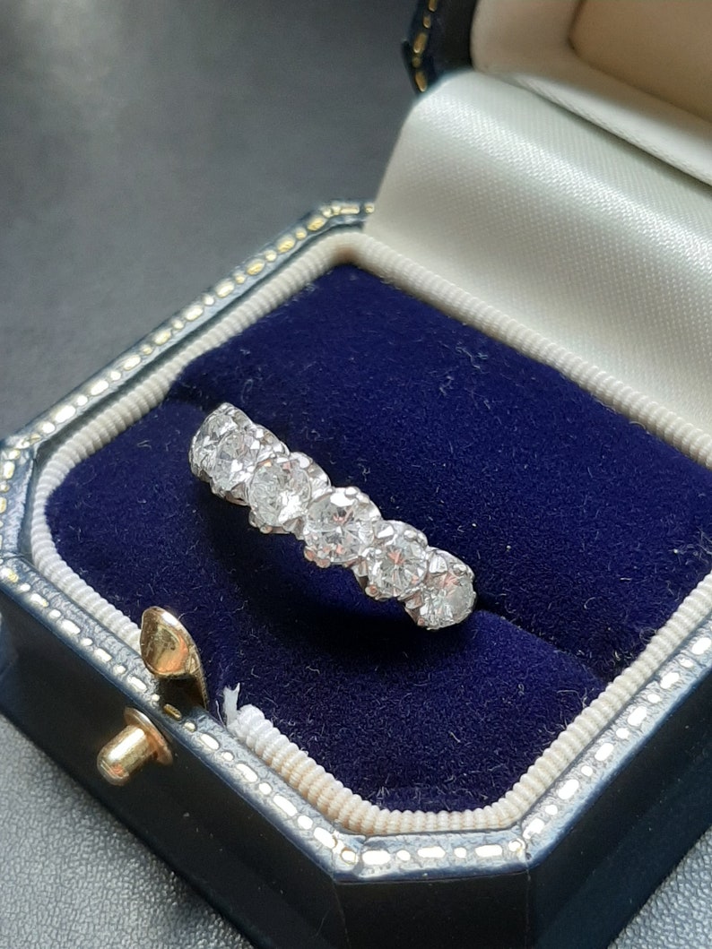 May include: A silver ring with a row of round, clear diamonds set in a band. The ring is in a blue velvet ring box.
