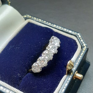 May include: A silver ring with a row of round, clear diamonds set in a band. The ring is in a blue velvet ring box.
