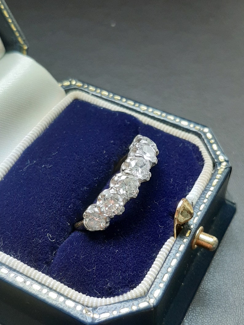 May include: A silver ring with a row of round, clear diamonds set in a band. The ring is in a blue velvet ring box.