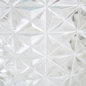 May include: Close-up of a clear glass vase with a geometric pattern. The vase has a diamond-shaped pattern that creates a textured surface.