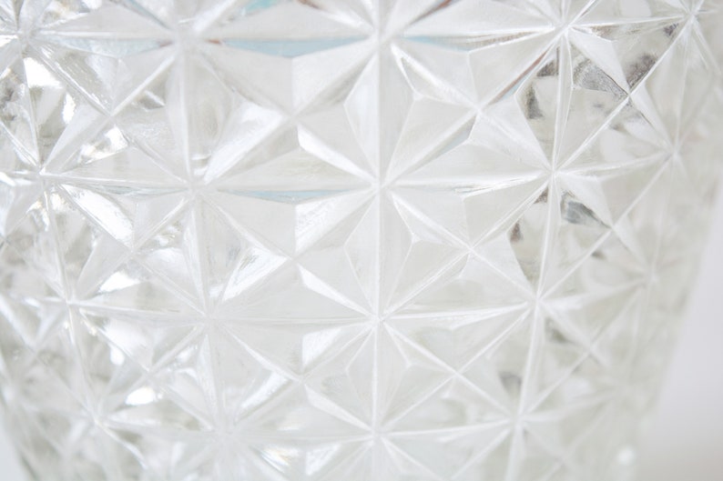 May include: Close-up of a clear glass vase with a geometric pattern. The vase has a diamond-shaped pattern that creates a textured surface.
