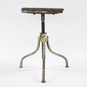 Puede incluir: Un taburete ajustable vintage con un asiento de madera y una base de metal pintada de verde y blanco. La base tiene un mecanismo de tornillo para ajustar la altura.
