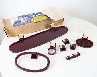 May include: A set of brown plastic bathroom accessories, including a soap dish, a toothbrush holder, a towel rack, and a shelf. The set is packaged in a cardboard box with the text "anbas istobal" printed on it.