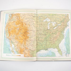 May include: Open book with a detailed map of the United States. The map features a color-coded topographic representation, with shades of brown and green indicating elevation. The Great Lakes and coastal regions are clearly visible.