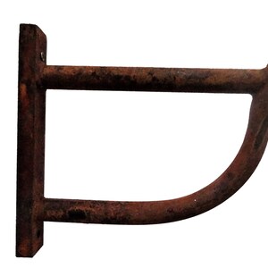 May include: A rusty metal wall-mounted hook with a curved arm. The hook is designed to hold items like coats, hats, or towels.